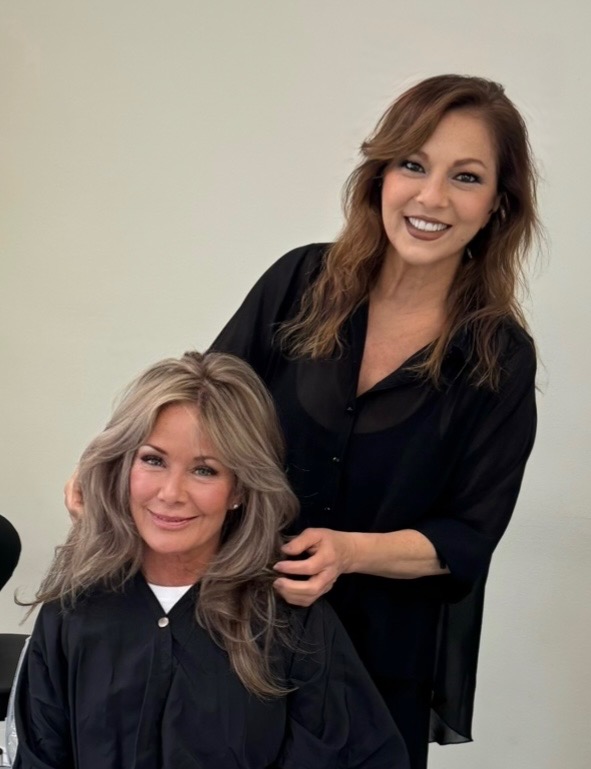 Cheta styling a client, smiling, hand in hair as finishing touch